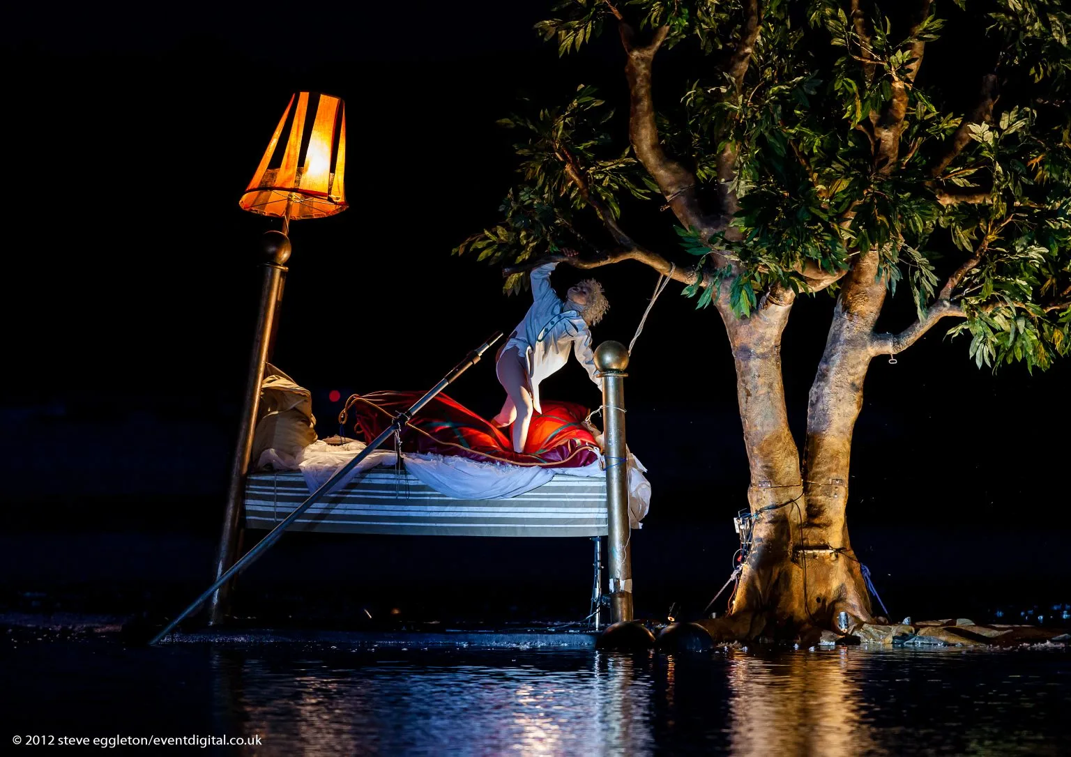 On the water, in a big bed a child hang on a branch of a floating tree. A picture from the ilotopie water show water fools