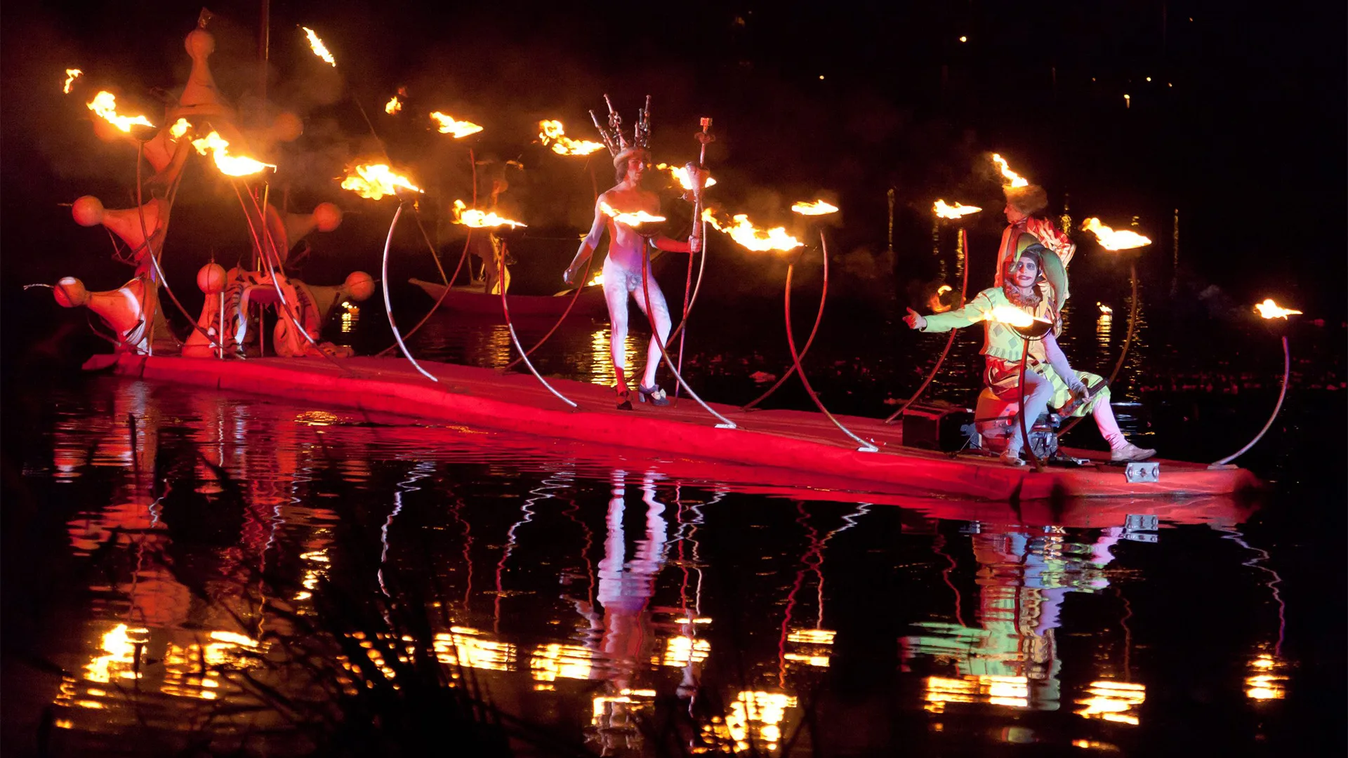 water theater by the ilotopie company, here a picture of the king carpet, a floating red carpet with fire, with a naked king an fool.