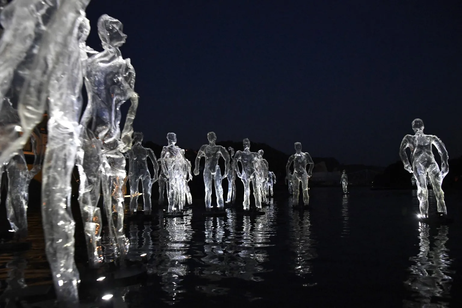 Floating enlighted transparent humain shells on deep dark water. A picture from the ilotopie company water show Drift here on the river La Seine in Rouen, France