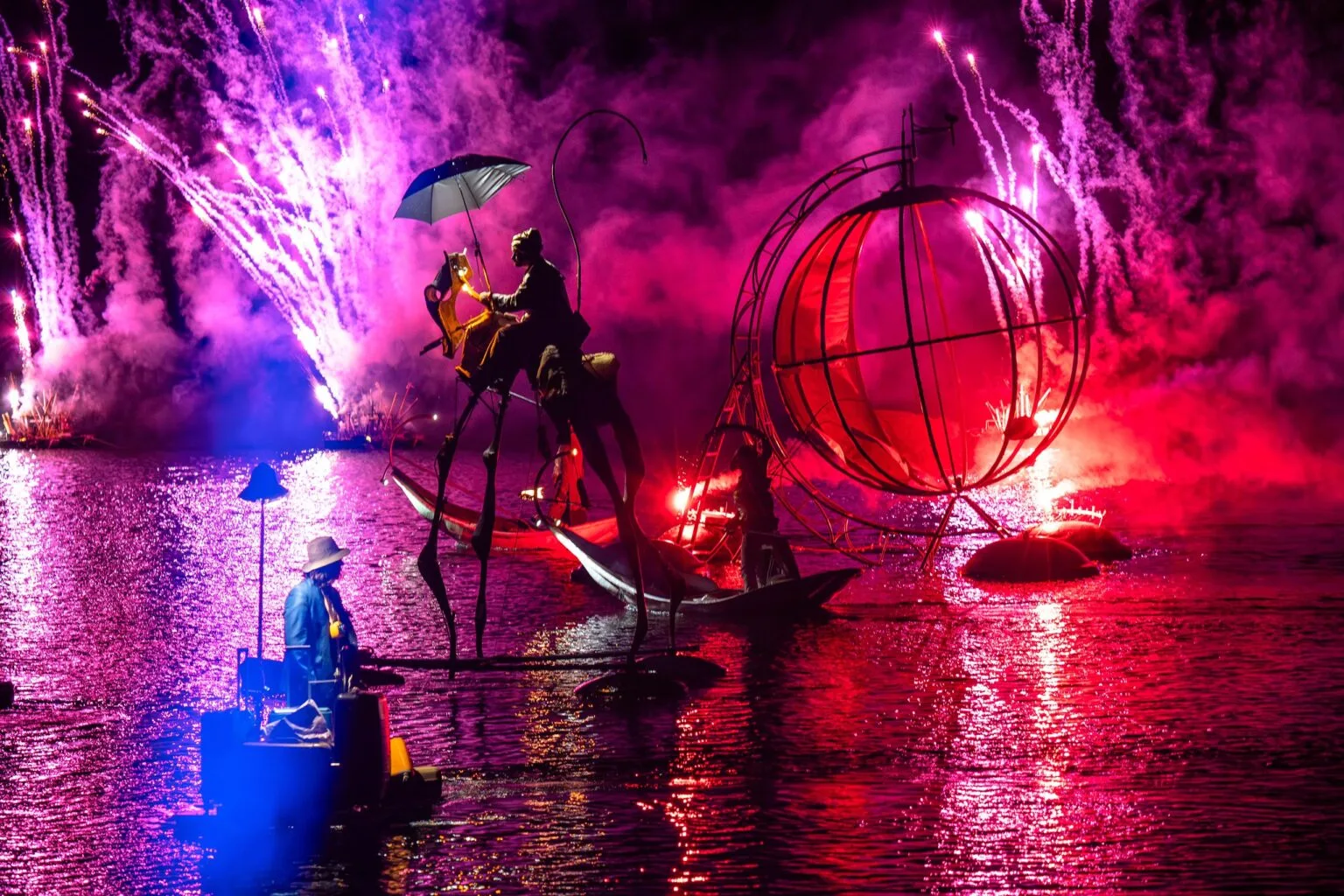 Une image d'un spectacle sur l'eau de la compagnie ilotopie. Le final des personnages sur des engins flottant, des feux d'artifice, un plan d'eau vaste.