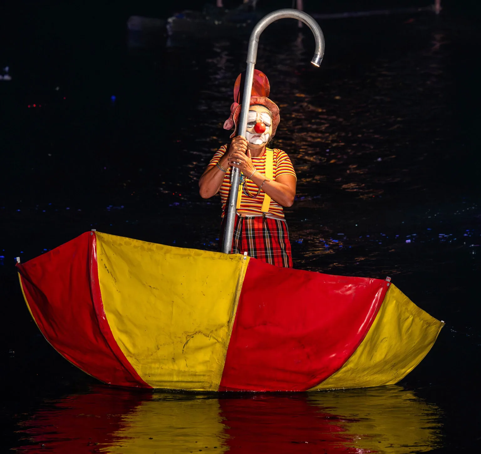 A clown in a big umbrella floating on the water. A picture come from the ilotopie water show The Extraodinary Journey.