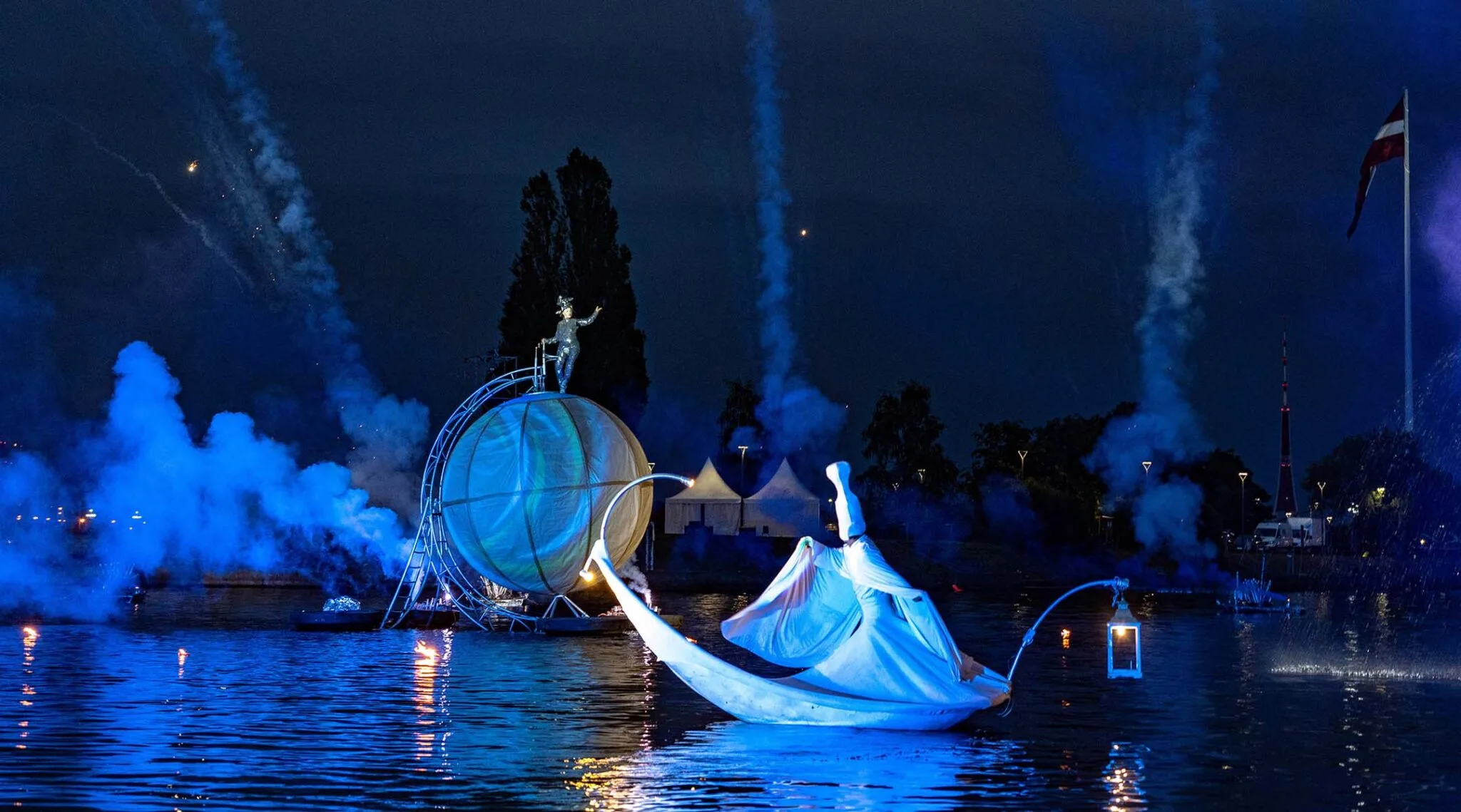 Pyrotechnic watershow The Extraordinary Journey, strange floating character and a giant sphere on the water, smoke, bleu light, deep night.