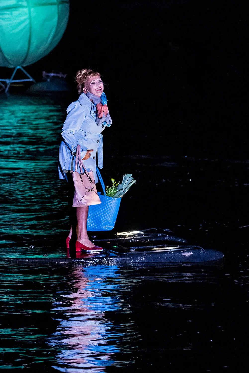 A smiling woman standing on water seems to come back from the market. A picture from the water show The Extraordinary Journey by the ilotopie company.