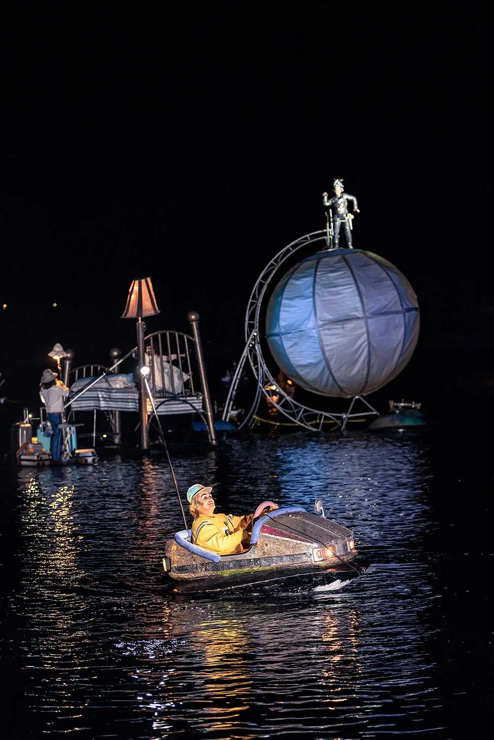 A floating bumper car, a floating tourist, a child on a big floating bed and a dancer on a big floating sphere. A picture take during The Extraodinary Journey, a water show by ilotopie company.