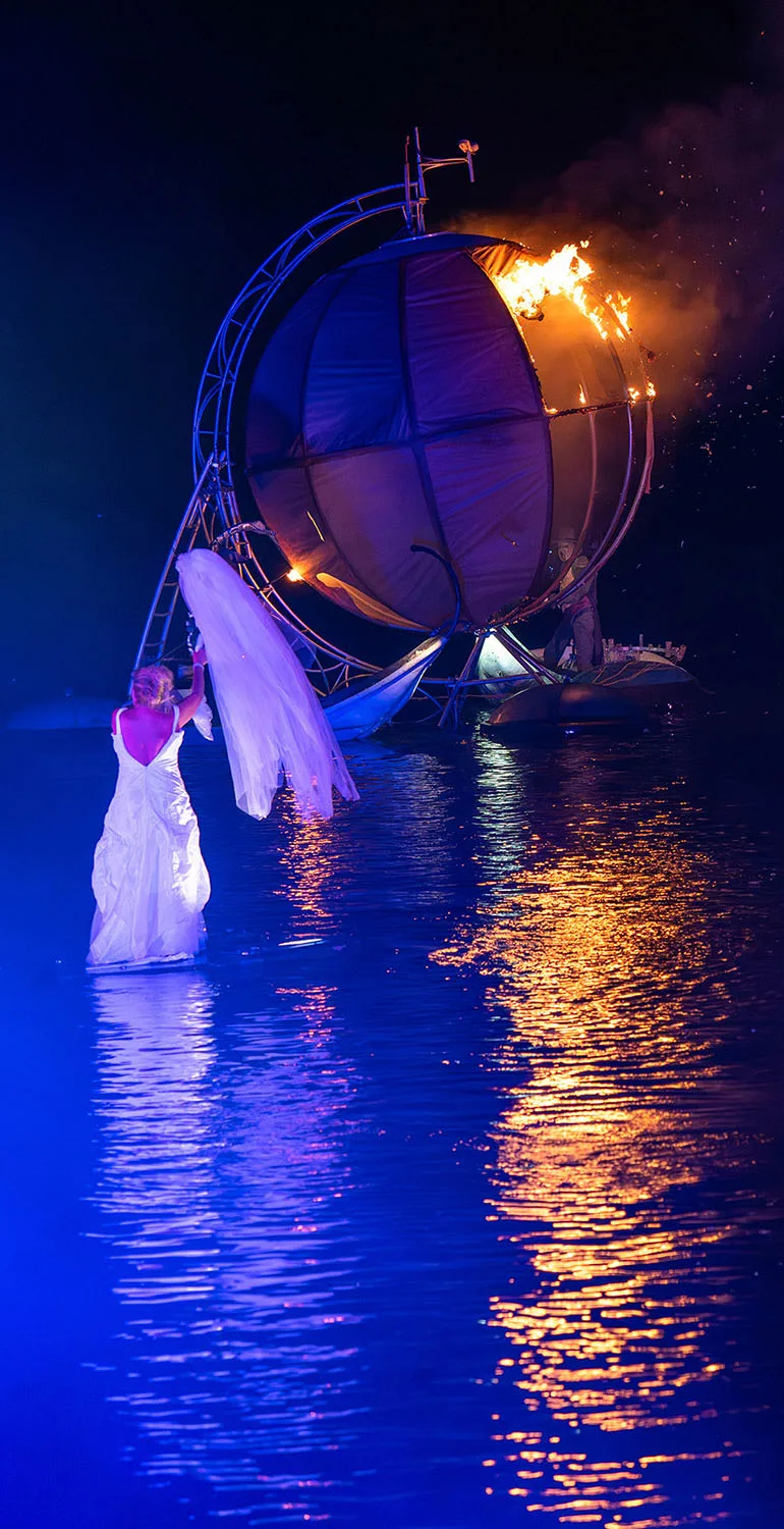 A floating bride on the water face a giant floating ball get on fire. A moment of the fantastic water show The Extraodinary Journey by the ilotopie company