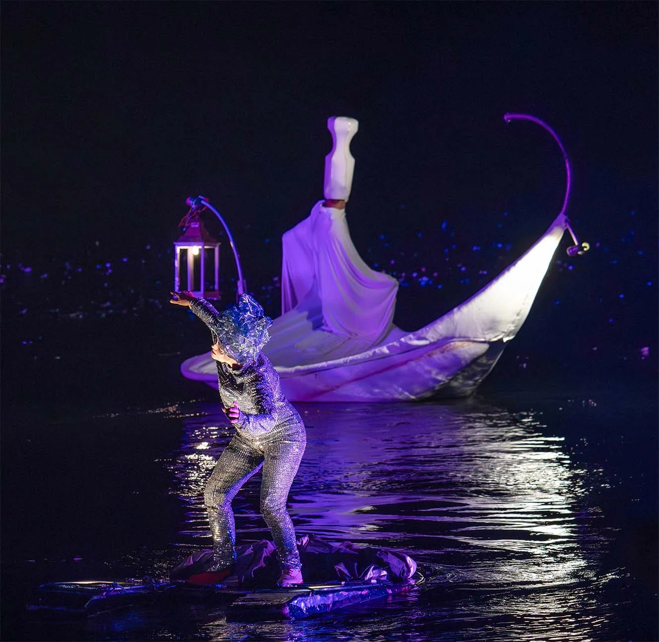 A silver character on a floating machine with a white character in a floating white petal on his back. An image of the ilotopie company water show the extraordinary Journey, here in Fos.